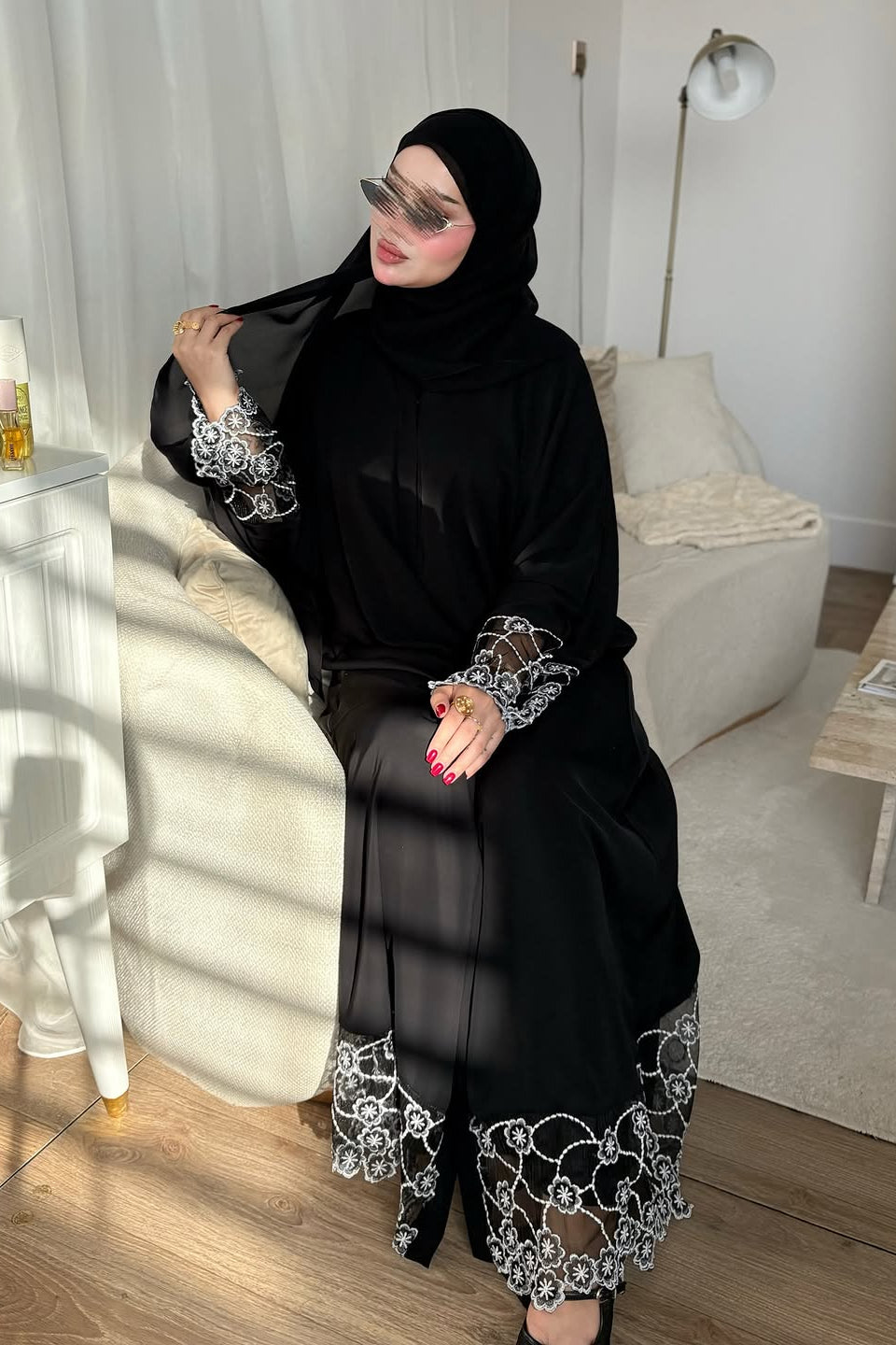 Woman in a black abaya with white embroidery in a living room.